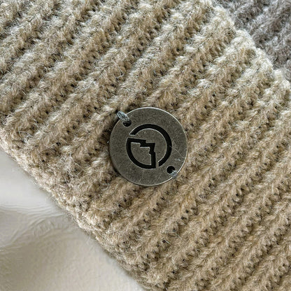 Close up of medallion on Domex Soft pink and taupe stripe cuffed beanie with a plush finish