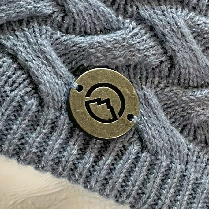 Close up of Domex medallion on  Dusty blue skullcap beanie with accent woven cable knit band 